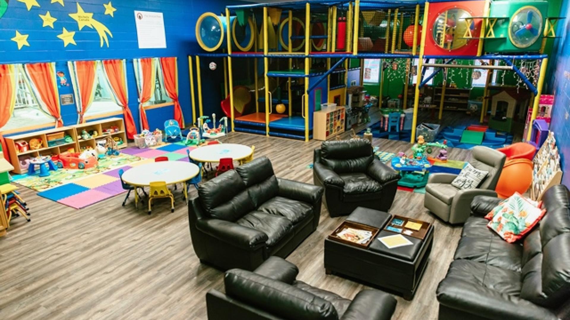 Playground interior. There are some tables, chairs, sofas and lounging chairs throughout the room. The room's paint scheme is bright and colourful.