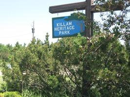 Signage for Heritage park. The sign is blue with white lettering. Trees surround the sign.